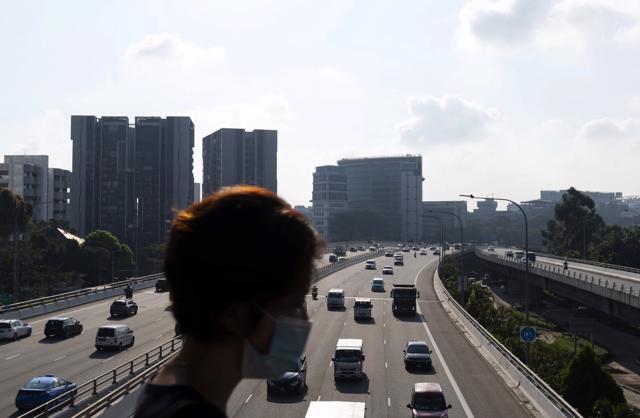 Một người phụ nữ đi qua c&acirc;y cầu ph&iacute;a tr&ecirc;n c&aacute;c phương tiện di chuyển dọc theo đường cao tốc Pan Island Expressway ở Singapore. Ảnh:Bloomberg.