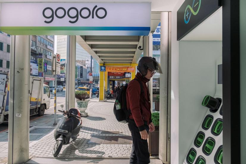 Một người đàn ông đứng cạnh trạm sạc pin của Gogoro Inc. bên ngoài một trong các cửa hàng của công ty này ở Đài Bắc. Ảnh: Bloomberg.