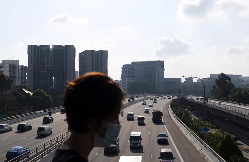 Một người phụ nữ đi qua cây cầu phía trên các phương tiện di chuyển dọc theo đường cao tốc Pan Island Expressway ở Singapore. Ảnh:Bloomberg.
