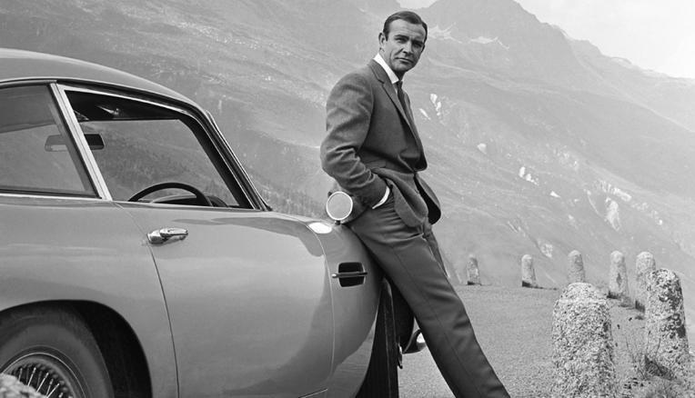 Diễn viên Sean Connery trong vai James Bond tạo dáng bên một chiếc Aston Martin DB5 trong một cảnh quay của phim “Goldfinger” (Ngón tay vàng) năm 1964.